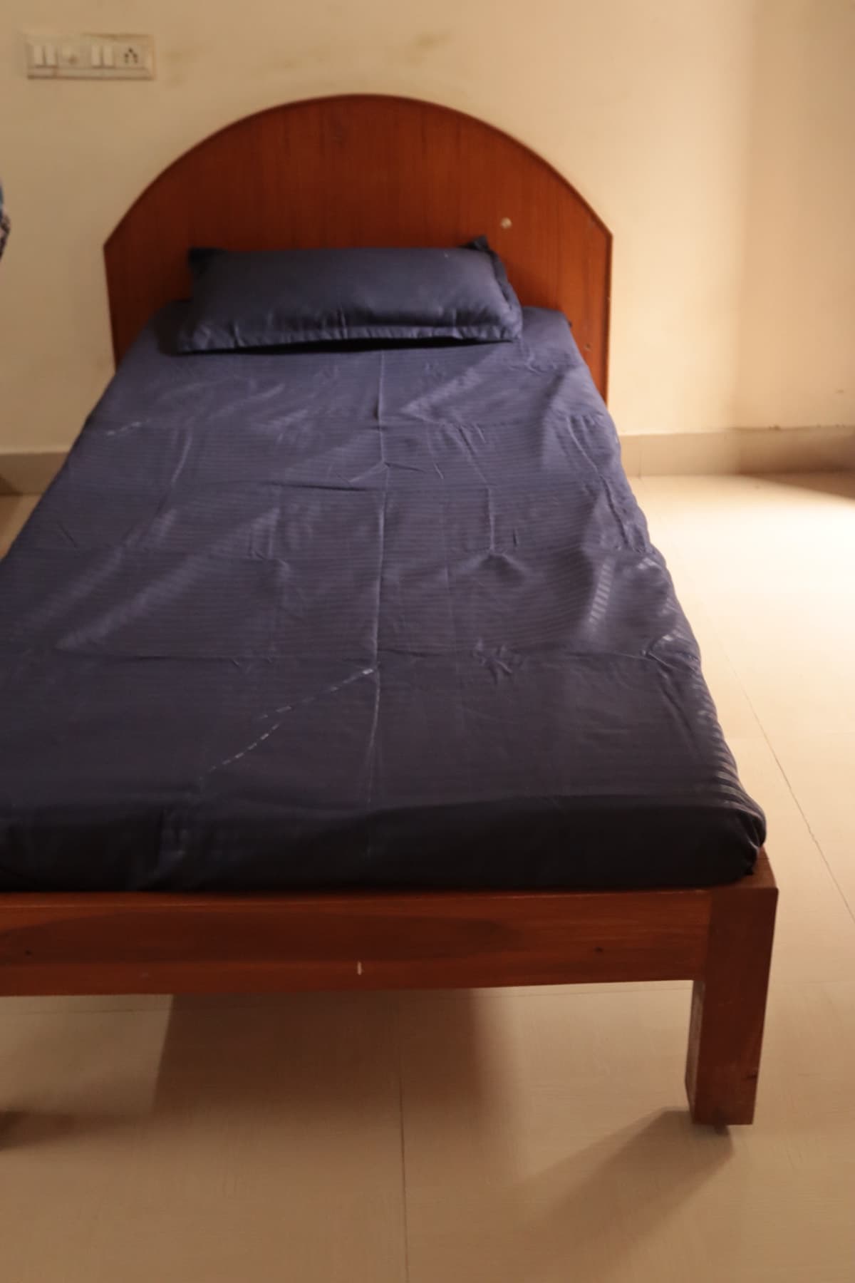 Single bed with wooden headboard in the Deluxe AC Triple Room